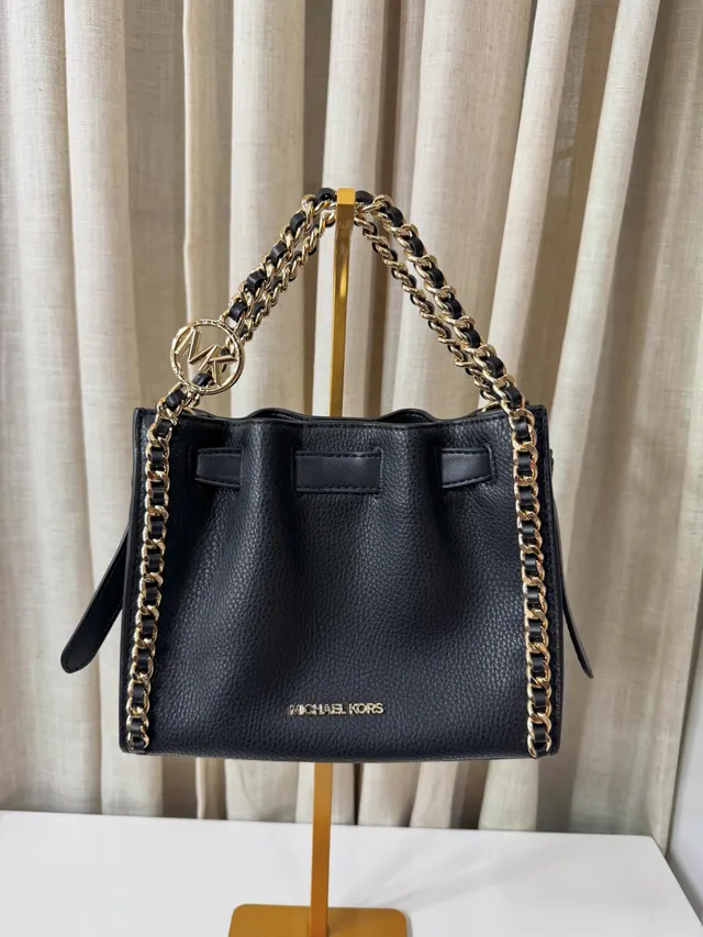 Bolso negro Michael Kors con cadena dorada colgado de un soporte dorado, de frente