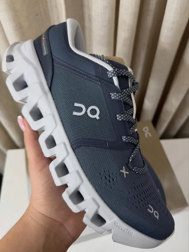 Zapatilla On Cloud X azul marino con suela blanca sostenida en la mano