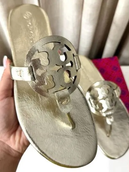Sandalia dorada metalizada Tory Burch sostenida en la mano